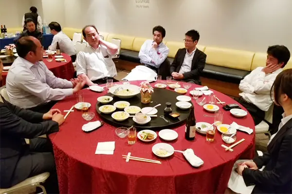 会社の食事会で8人の社員が円卓を囲んで話している様子